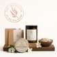 ustralian olive oil soap products including a bar, balm, and candle on a wooden stand with flowers.