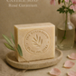 Bar of olive oil soap with 'The Australian Olive Oil Soap' branding, placed on a stone surface with flowers and petals.