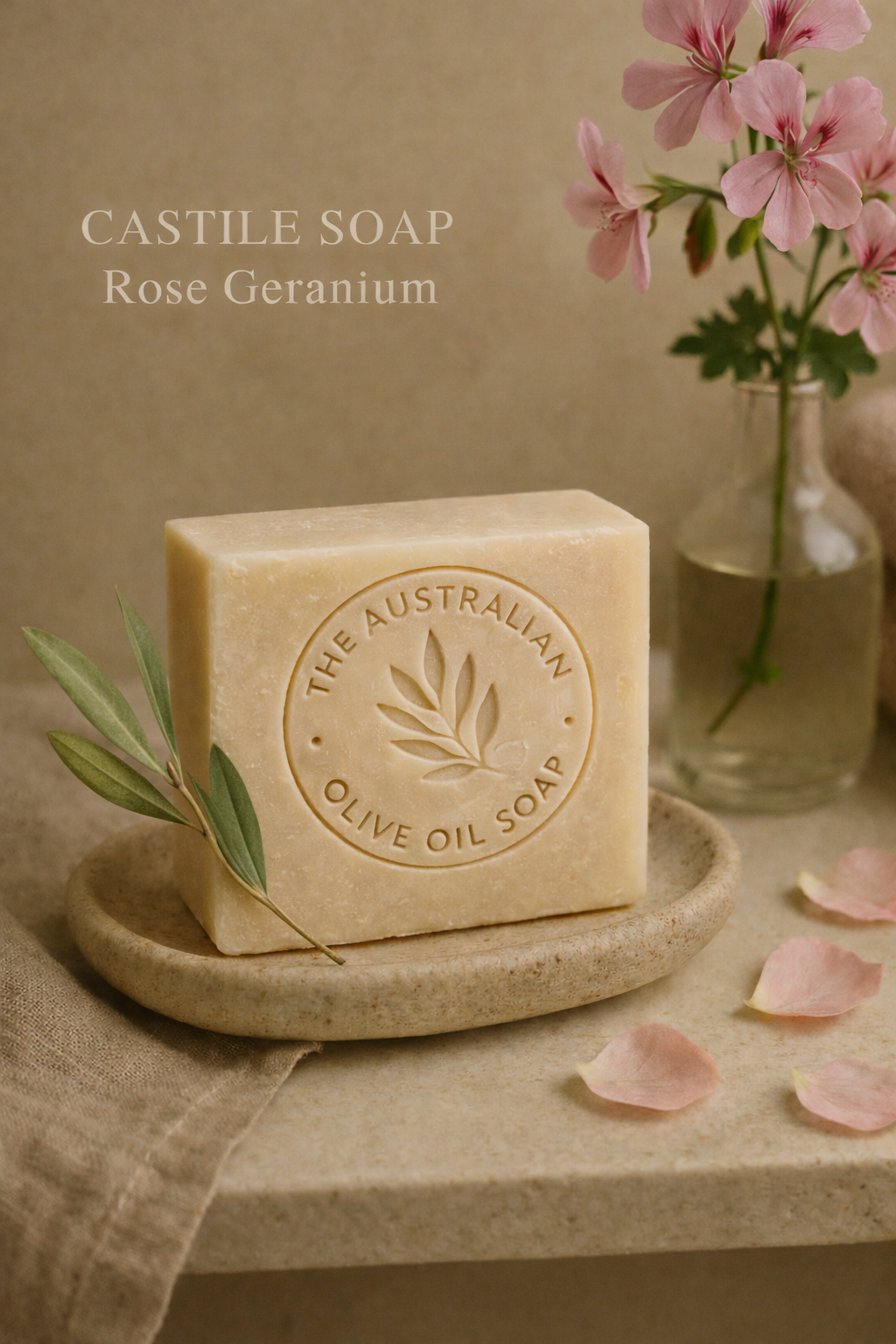Bar of olive oil soap with 'The Australian Olive Oil Soap' branding, placed on a stone surface with flowers and petals.