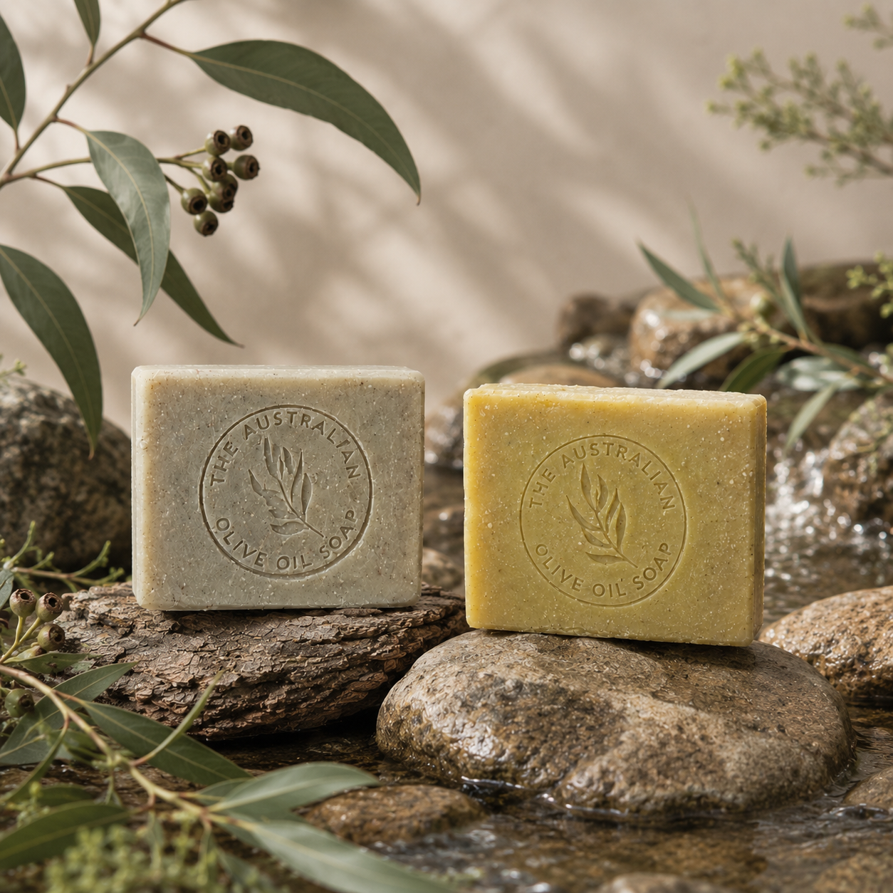 Two bars of soap from 'The Australian Olive Oil Soap.' on rocks with greenery in the background