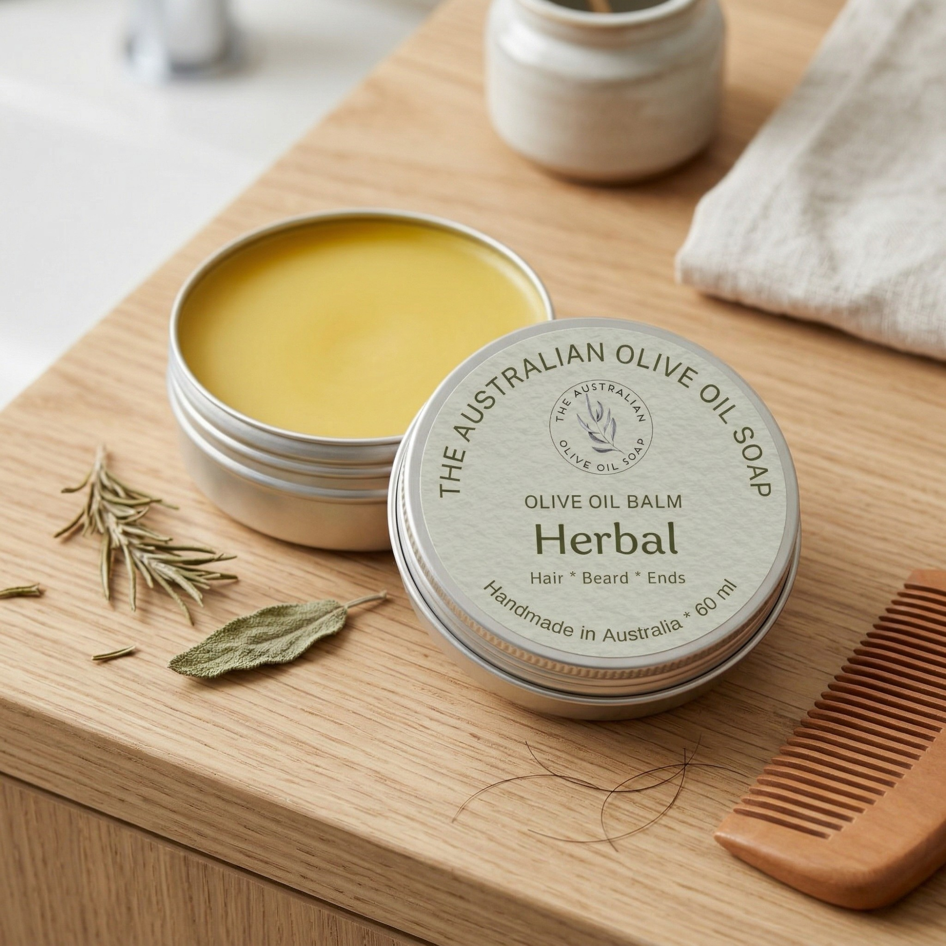 Olive oil balm in a tin with a wooden comb and herbs on a wooden surface